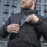Mies pukeutuneena M-Tac Rubicon Jakke Gen. II -takkiin, näyttää takin kestävän Cordura-kankaan ja käytännöllisen rintataskun kaupunkiympäristössä.